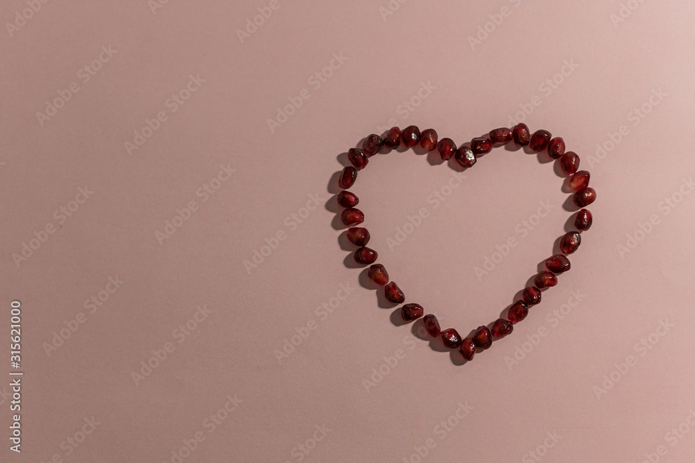Heart made from pomegranate seeds, unfilled, with a light shadow on a pink background. Horizontal top view