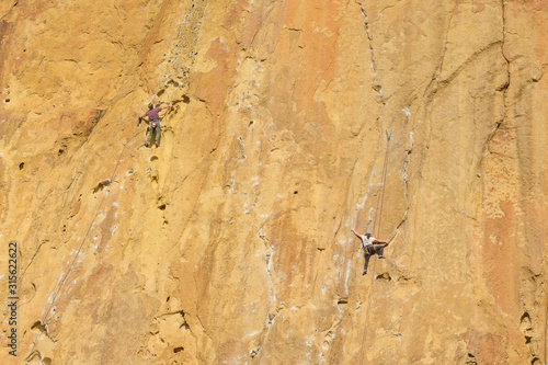 Climbers climb a large rock  filmed from the back. With space