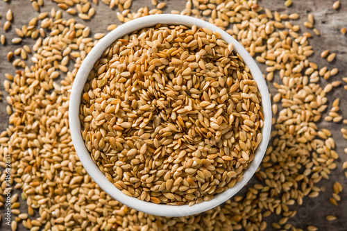 Golden flax seeds in white bowl on wooden table. Top view