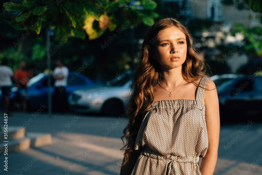 Close-up a young beautiful woman who stands in the street, people and cars in the background Close-up a young beautiful woman who stands in the street, people and cars in the background