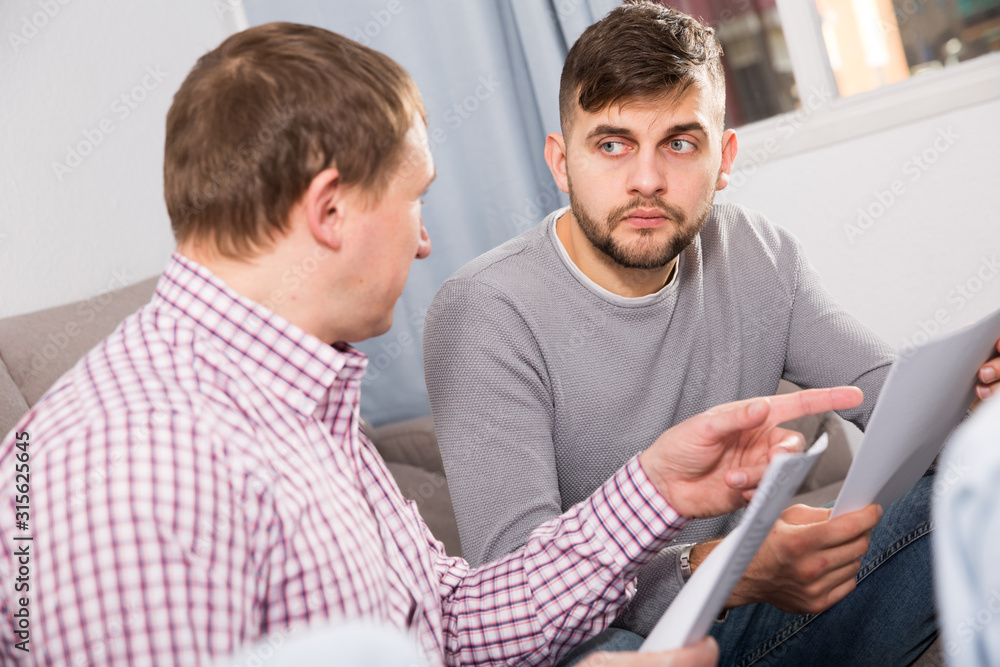 Upset man with friend looking at papers on sofa