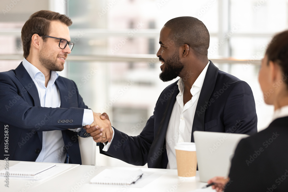 Diverse male partners handshake closing deal at meeting Diverse male partners handshake closing deal at meeting