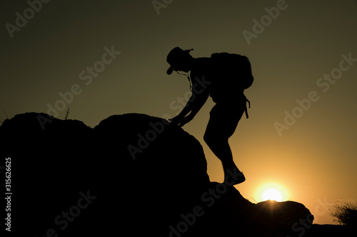 Silhouette of man climbing at sunset
