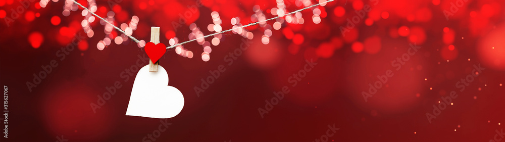 Happy Valentine's Day background banner panorama - White heart hang on wooden clothes pegs with wooden heart and bokeh lights on a string isolated on red texture, with space for text - obrazy, fototapety, plakaty 