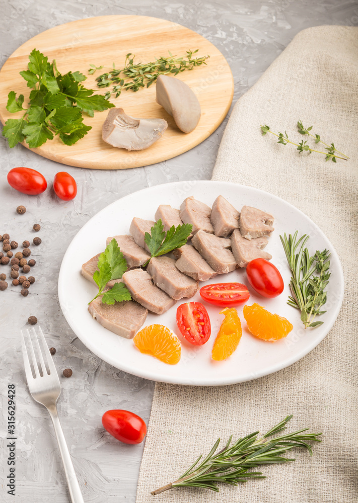 Boiled pork tongue with tomatoes and herbs on a gray concrete background. Side view, close up.