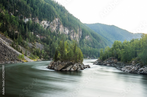 Rocky island covered by spurce trees in summer early morning. Confluence of the mountain rivers Balyiktyig hem and Kyzil hem, Siberia, Russia. Long exposure. photo