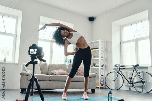 Full length of flexible young African woman working out while making social media video