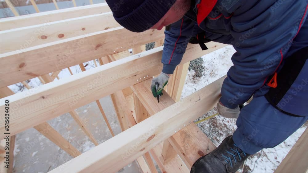 Builder is measuring wooden beam with measuring tape and writing numbers on it. Frame house building Builder is measuring wooden beam with measuring tape and writing numbers on it. Frame house building