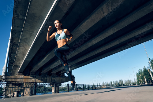 Sporty woman running outdoors under city bridge