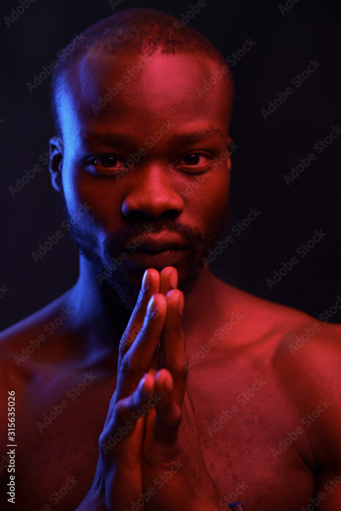 portrait of a black guy with a naked torso on a dark background with a red light he holds his hands in front of him and looks into the camera portrait of a black guy with a naked torso on a dark background with a red light he holds his hands in front of him and looks into the camera