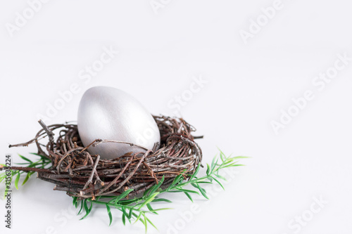 Easter holiday composition. Silver-colored egg in a nest of twigs on a white background. Easter flat lay. Copyspace.