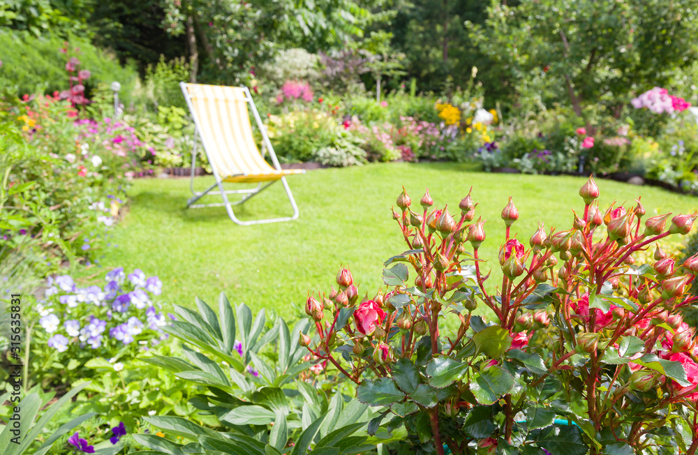 Garden chair on a green lawn in a beautiful flower garden in summer. Shallow dept-of-field, deck chair is out of focus Garden chair on a green lawn in a beautiful flower garden in summer. Shallow dept-of-field, deck chair is out of focus
