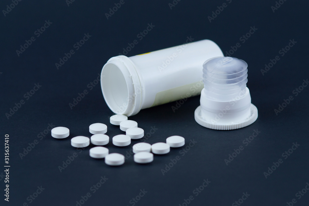 Cylindrical tube with scattered tablets and a cap on a gray background.