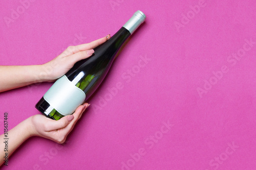 woman hands hold bottle of wine on purple colored paper background top view with copy space