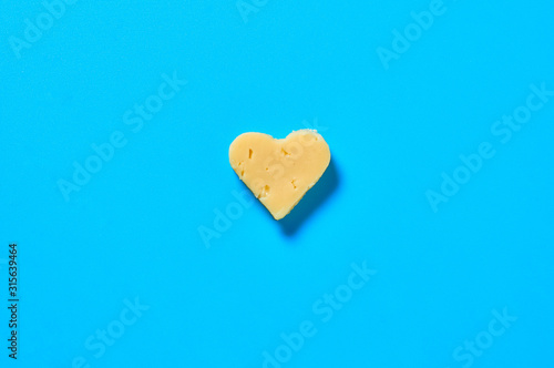 Piece of cheese in form of heart lies on blue desk on kitchen. Concept of Valentine's Day. Top view. Close-up