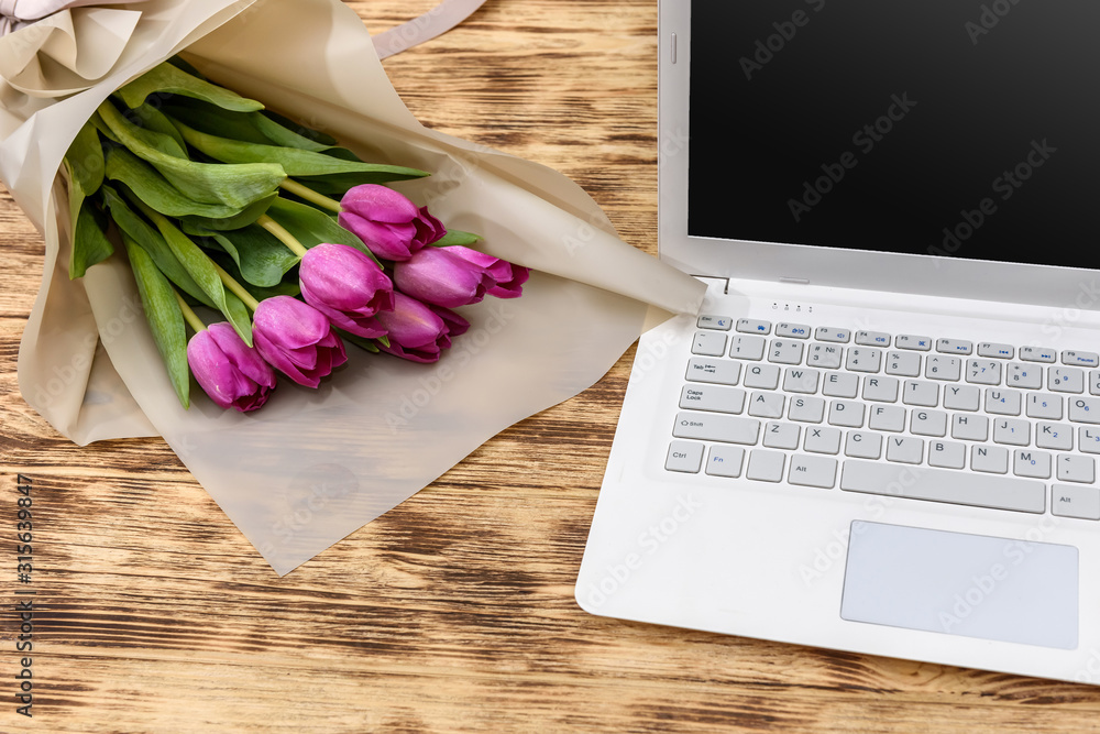 Bouquet of tulips and laptop on wooden table