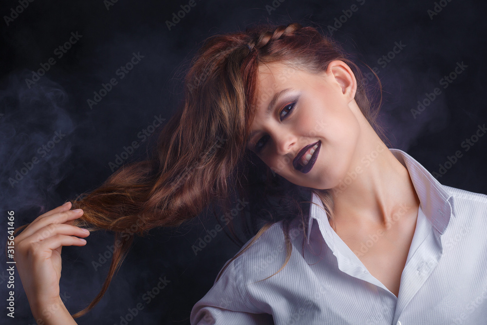 Beautiful young girl with creative dark make-up on dark background in the smoke. Long, well-groomed hair. Beautiful young girl with creative dark make-up on dark background in the smoke. Long, well-groomed hair.