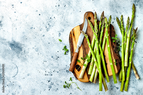 Bunch of fresh green asparagus on wooden board with seasonings. Top view, copy space photo