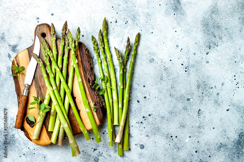 Bunch of fresh green asparagus on wooden board with seasonings. Top view, copy space