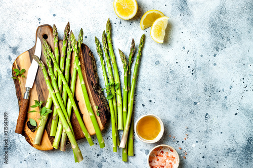 Bunch of fresh green asparagus on wooden board with olive oil, lemon and seasonings. Top view, copy space