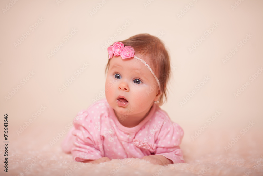Cute little baby girl in a pink dress with a spring wreath on her head with big blue eyes in the Studio in a high key. Emotion-surprise. Concept: baby care, baby food, baby health. Cute little baby girl in a pink dress with a spring wreath on her head with big blue eyes in the Studio in a high key. Emotion-surprise. Concept: baby care, baby food, baby health.