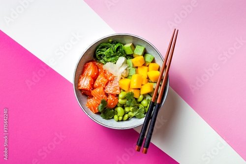 Hawaiian salmon poke bowl with seaweed, avocado, edamame, mango and pickled ginger. Top view, bright pink background photo