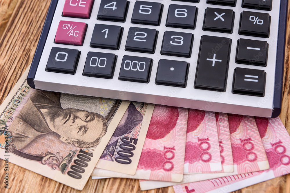 Calculator with chinese and japanese banknotes on wooden background close up Calculator with chinese and japanese banknotes on wooden background close up