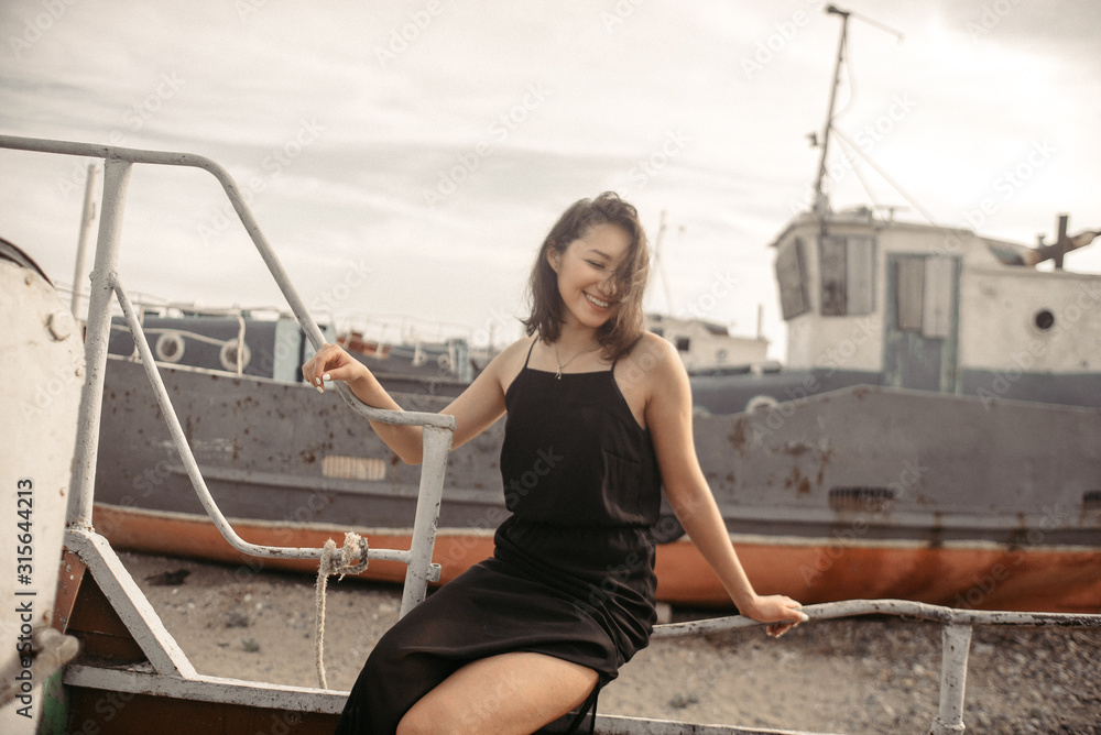 Obraz premium Woman in black dress on beach with broken ships