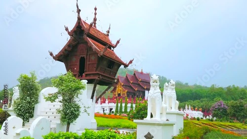 The stilt wooden mondop (pavilion) of Buddhist shrine with carved pyathat roof, surrounded by white Singha lions, located at the Roayal Pavilion of Rajapruek Royal Park in Chiang Mai, Thailand photo