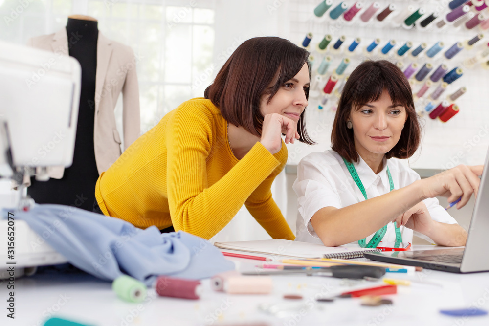 Fototapeta premium Two young female dressmakers working in sewing studio. Sisters start family business. Bespoke tailoring. Private enterprise. Hobby and business