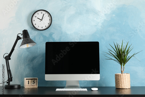 Workplace with computer, plant and lamp on wooden table. Light blue background photo