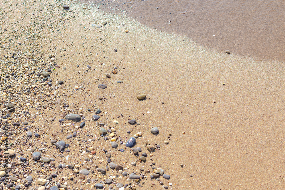 Background of wet sand with pebbles after the departure of the coastal wave