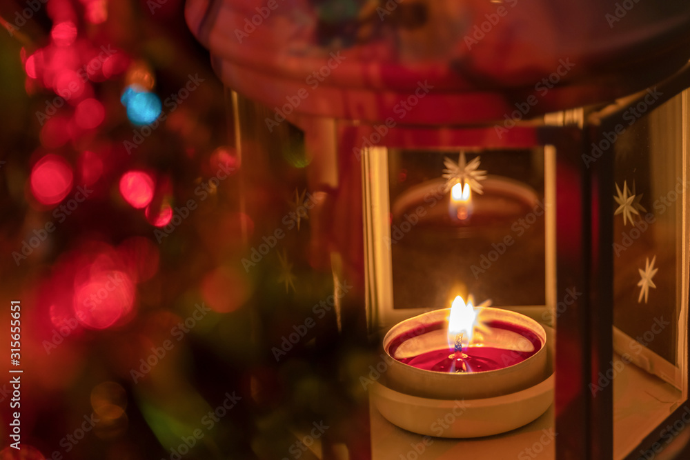Festive Christmas candle in a lamp on a blurry colorful dark background with multi-colored lighting with bokeh. Focus with shallow depth of field. Festive Christmas candle in a lamp on a blurry colorful dark background with multi-colored lighting with bokeh. Focus with shallow depth of field.