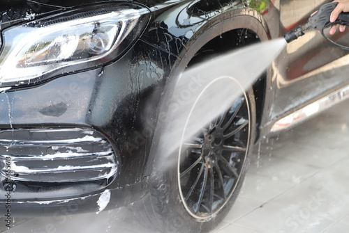 Closeup of black car cleaning, washing with high pressure water spraying.