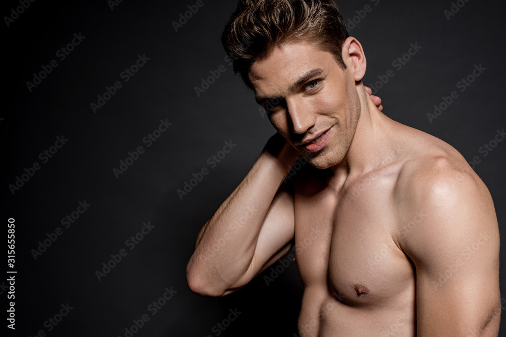 smiling sexy young naked man with muscular torso posing on black background