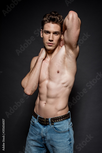 sexy young man with muscular torso in jeans posing on black background