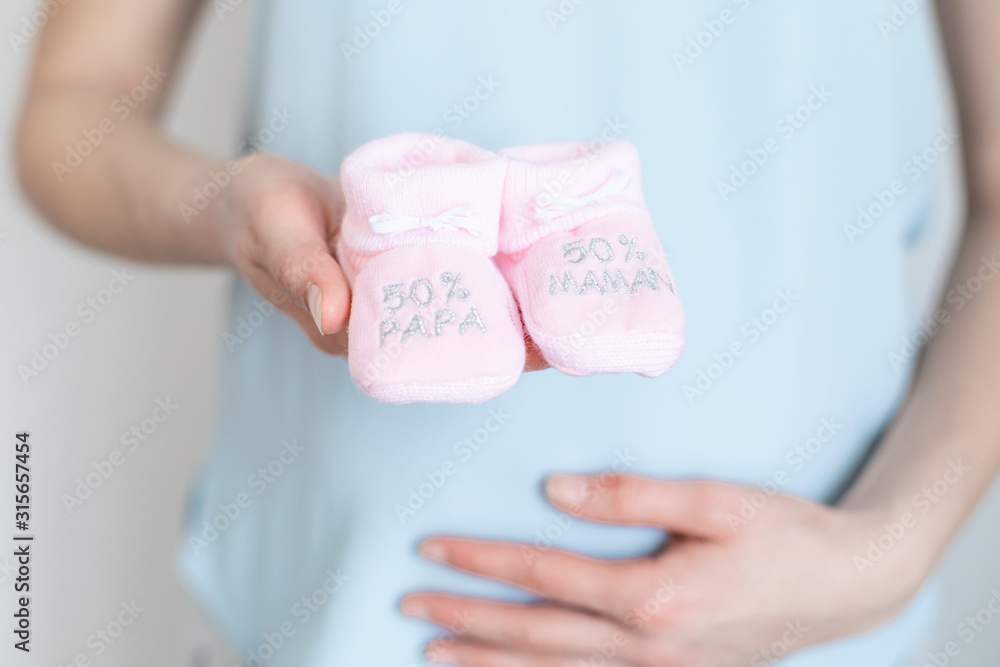 young pregnant woman with baby booties in hands - 50% Dad 50% Mum - Gender reveal young pregnant woman with baby booties in hands - 50% Dad 50% Mum - Gender reveal