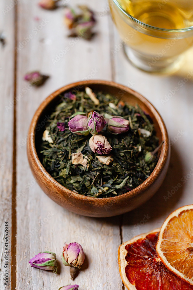 Natural organic dry leaves of green tea with rose flowers and fruits in wooden bowl. Traditional source of relaxation and detention, atmosphere of spa. Healthy and delicious beverage Natural organic dry leaves of green tea with rose flowers and fruits in wooden bowl. Traditional source of relaxation and detention, atmosphere of spa. Healthy and delicious beverage
