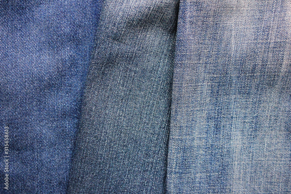 Naklejka premium Jeans background of blue denim clothing. Three pairs of various jeans, light and dark blue denim fabric textures, empty old trousers wallpaper 