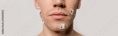 cropped view of naked man with bloody wounds after shaving on face isolated on grey, panoramic shot