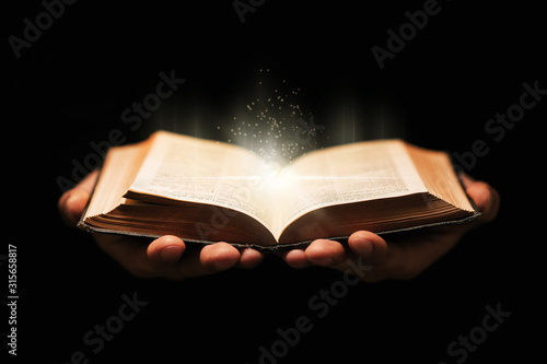 Tablou canvas Man holds holy bible book on black background.