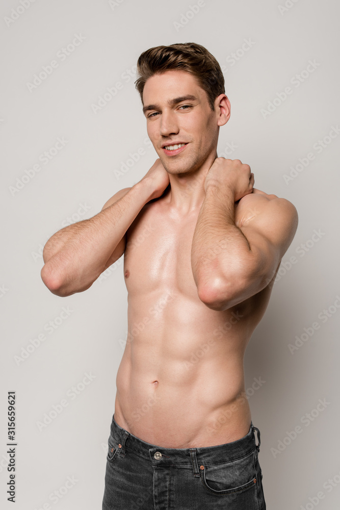 smiling sexy man with muscular torso posing isolated on grey