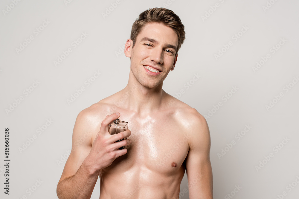 smiling sexy man with muscular torso spraying perfume isolated on grey smiling sexy man with muscular torso spraying perfume isolated on grey