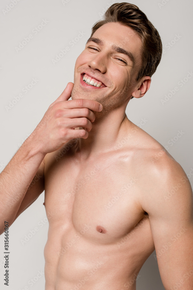 smiling sexy man with muscular torso touching chin isolated on grey smiling sexy man with muscular torso touching chin isolated on grey