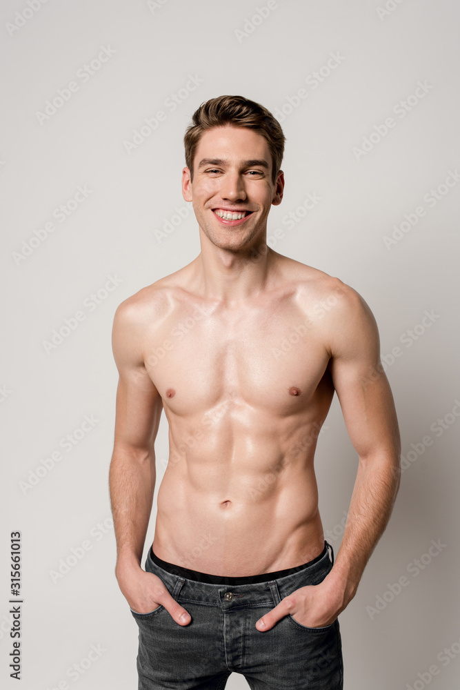 smiling sexy man with muscular torso with hands in pockets isolated on grey smiling sexy man with muscular torso with hands in pockets isolated on grey