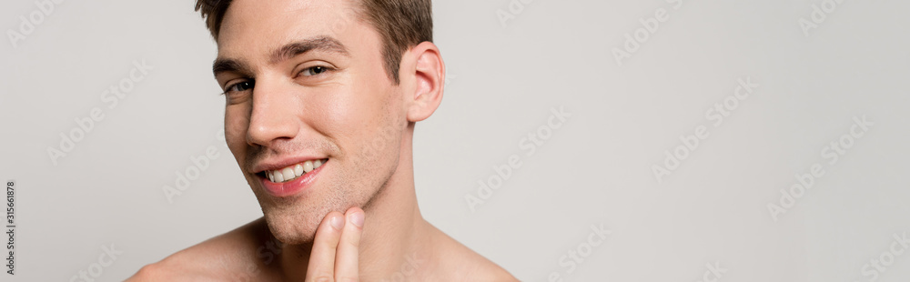 smiling naked sexy young man touching skin isolated on grey, panoramic shot smiling naked sexy young man touching skin isolated on grey, panoramic shot