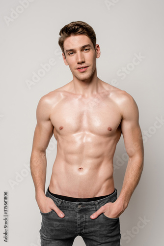 sexy man with muscular torso and hands in pockets isolated on grey