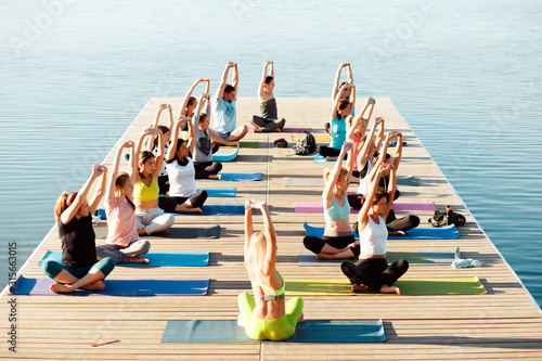 A big group of people attending yoga classes on a pontoon near the lake.