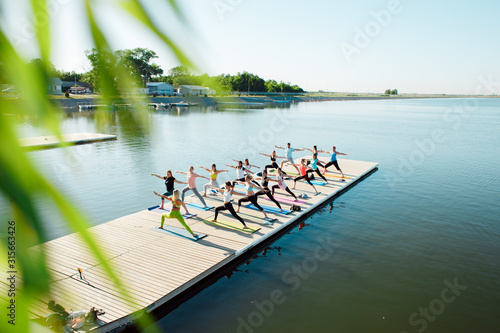 A big group of people attending yoga classes on a pontoon near the lake.