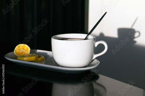 a pottery white cup on a black table and its shadow from the bright sun  tea break with lemon